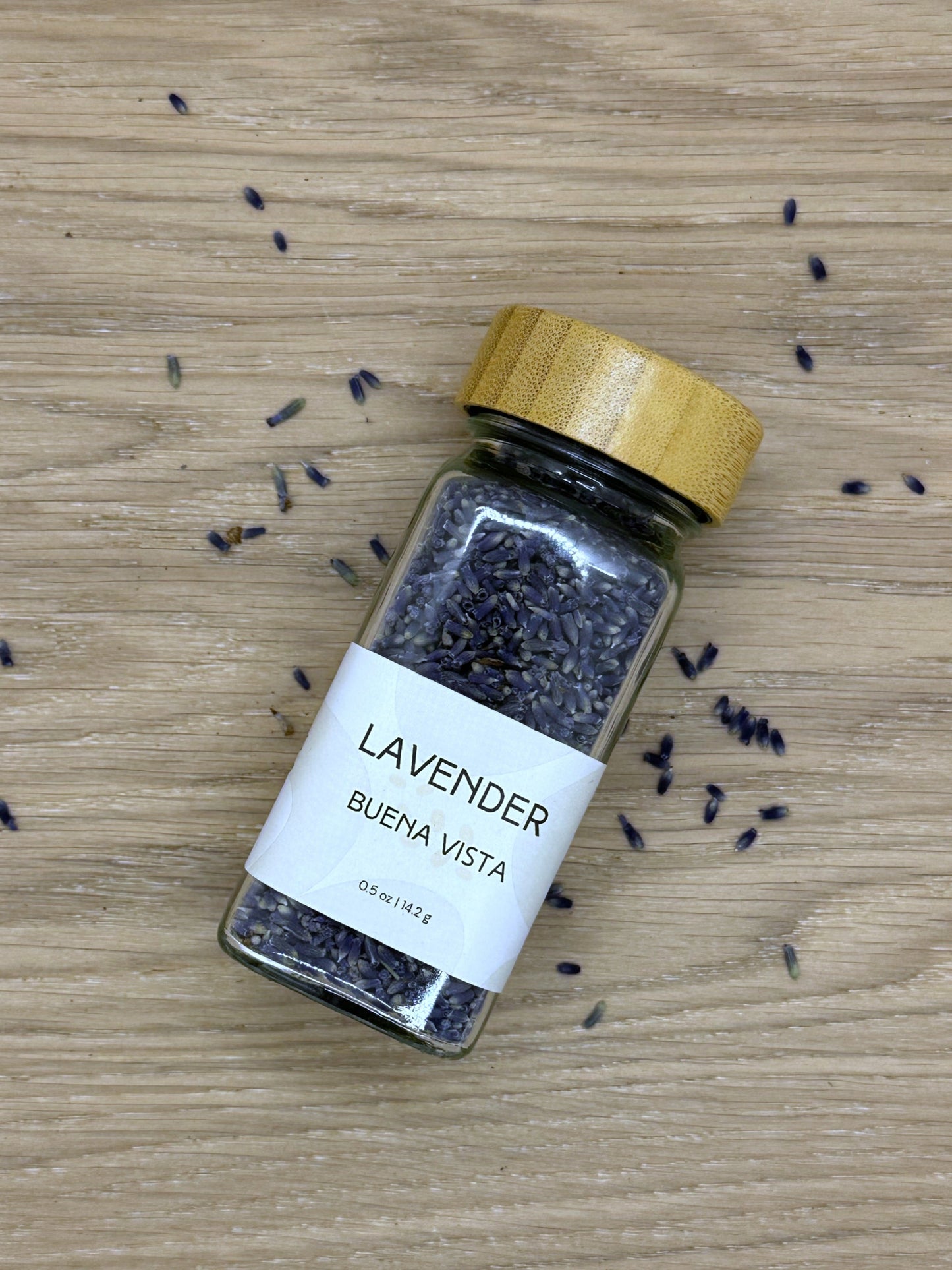 Bottle of lavender on a wooden surface with scattered lavender buds.