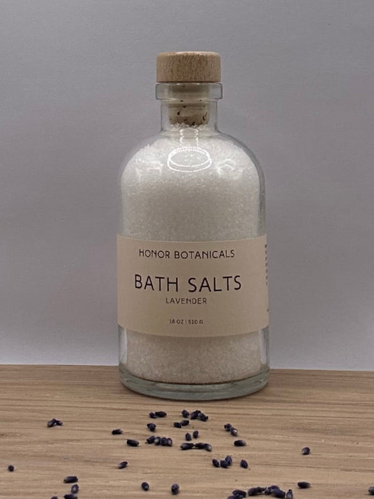 Bottle of bath salts on a wooden surface with scattered lavender buds and gray background