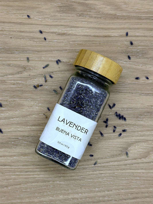 Bottle of lavender on a wooden surface with scattered lavender buds.