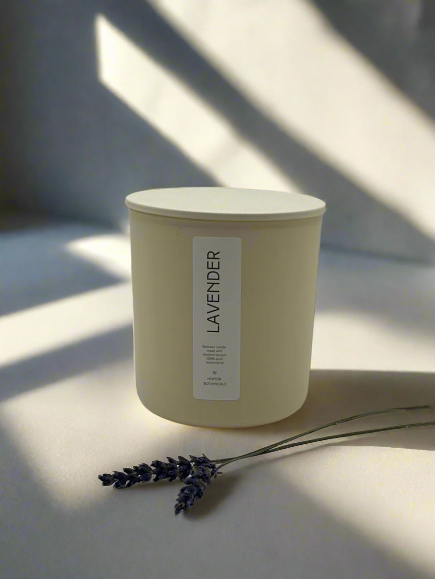 Lavender candle with a label on a light surface with shadows and a few sprigs of dried lavender