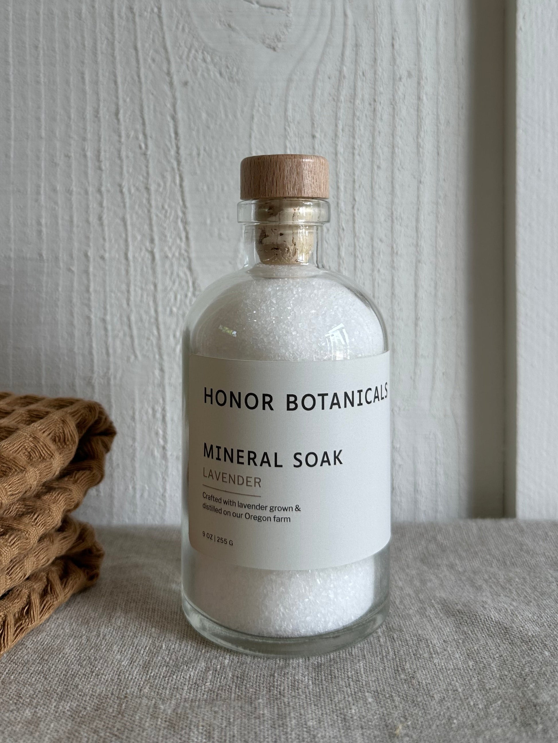 Bottle of Honor Botanicals Mineral Soak on a wooden surface with a textured mat in the background